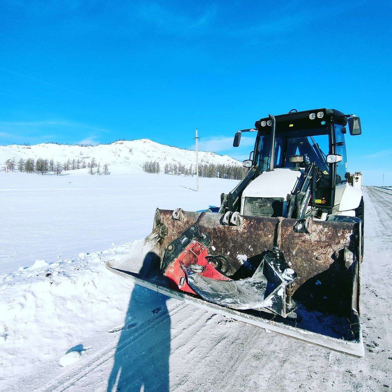 Экскаватор-погрузчик с отвалом на зимней дороге в Учалах